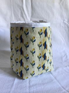 a close up of a small basket on a white cloth covered surface with birds and flowers