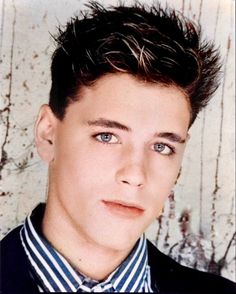 a young man with short hair and blue eyes wearing a striped shirt, bow tie and black blazer