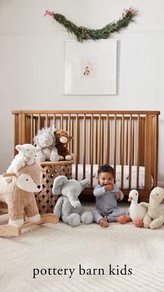 a baby sitting on the floor in front of stuffed animals and a wooden crib