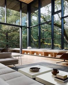 a living room filled with furniture and lots of windows overlooking the trees in the forest