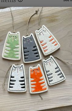 six ceramic cat ornaments hanging from strings on a wooden surface with text overlay that says,