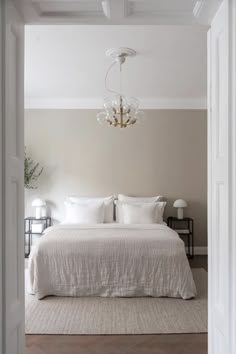 a white bed sitting under a chandelier in a bedroom