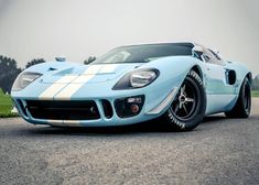 a blue and white sports car parked on the street in front of a grassy area