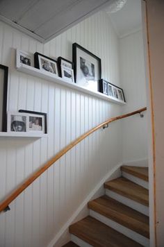 the stairs are lined with pictures and framed photographs on white wall paneling, along with wooden handrails