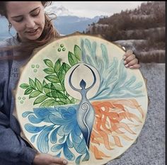 a woman holding a painted plate in her hands