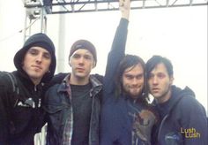 four young men posing for the camera with their arms in the air and one holding his hand up