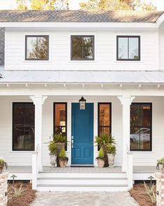 a white house with blue front door and two planters on the steps next to it