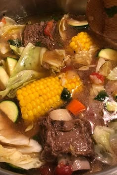 a pot filled with stew and vegetables on top of a stove next to a wooden spoon