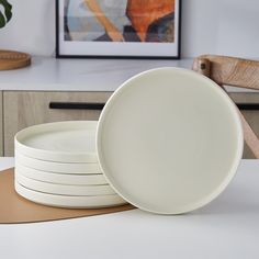 four white plates stacked on top of each other in front of a wooden board and plant