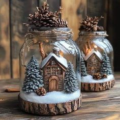 two glass jars filled with snow and pine cones on top of a wooden table next to each other