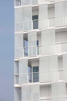 an airplane is flying in the sky near a tall white building with balconies