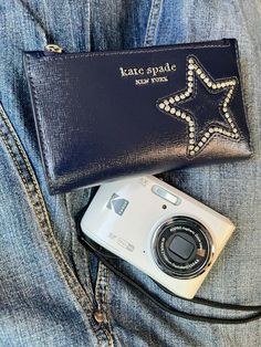 a camera sitting on top of a blue jean jacket next to a purse that says kate spade