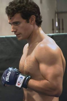 a shirtless man wearing boxing gloves and holding a punching mitt in his right hand