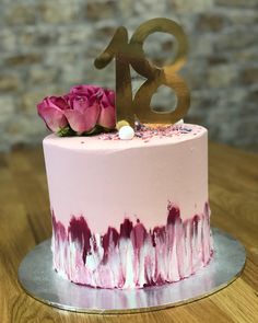 a pink and white cake with gold numbers on top sitting on a wooden table next to a brick wall