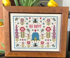 a wooden frame holding a cross - stitch pattern with flowers and bee happy on it