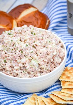 a white bowl filled with tuna salad next to crackers on a blue and white towel