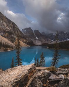 a lake surrounded by mountains and trees under a cloudy sky with some clouds in the background