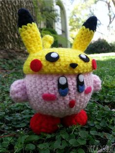 a crocheted pokemon pikachu hat sitting on top of green grass next to a tree