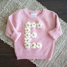 a pink sweater with white flowers on it and the letter e spelled out in large letters