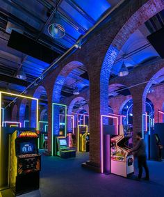 a man playing an arcade game in a large room with neon lights on the walls