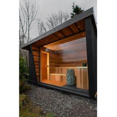 an outdoor saunace with wooden walls and windows on gravel ground next to trees