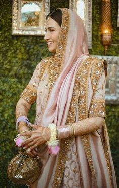 a woman in a pink and gold bridal outfit holding a bag with flowers on it