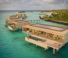 an aerial view of some houses in the middle of blue water with palm trees on either side