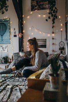 a woman sitting on top of a bed holding a cup of coffee in her hand