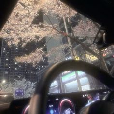 the dashboard of a car in front of some tall buildings at night time with cherry blossoms on trees