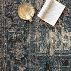 an open book on top of a rug next to a gold plate and coffee cup