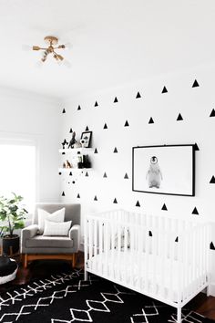 a baby's room decorated in black and white with triangles on the wall, crib, chair, and rug