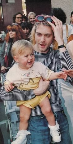 a man holding a baby in front of a group of people with sunglasses on their heads