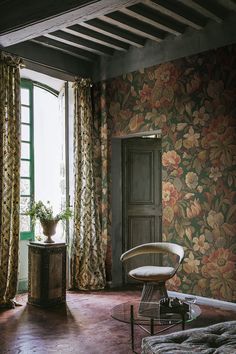 a living room with floral wallpaper and curtains on the window sill, next to a chair