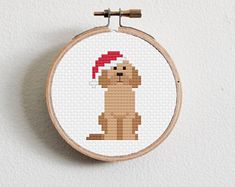 a cross stitch dog with a santa hat on it's head sitting in front of a white wall