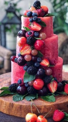 a watermelon cake with berries and cherries on the top is sitting on a wooden platter