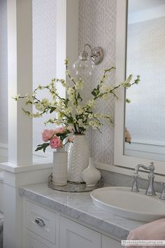 a white vase filled with flowers on top of a bathroom counter