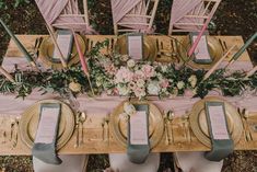 an overhead view of a table set with gold plates and place settings, pink napkins and floral centerpieces