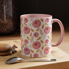 a pink coffee mug sitting on top of a wooden cutting board next to a spoon