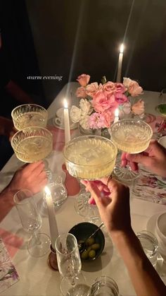 people are toasting at a table with wine glasses and flowers in the center, surrounded by candles