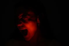 a woman is screaming in the dark with red light on her face and mouth open