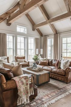 a living room filled with lots of furniture next to large windows and wooden beamed ceilings