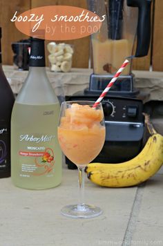 an orange drink in a wine glass next to two bottles of alcohol and a banana