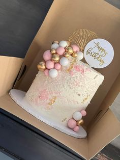 a white cake with pink and gold decorations in a box on top of a table