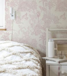 a white bed sitting next to a wall with pink flowers on it's side