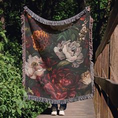 a woman walking down a wooden walkway carrying a blanket with flowers on it and tassels around the edges