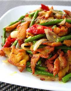 a white plate topped with green beans, onions and fried meats covered in sauce