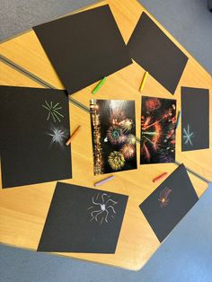 some pictures and pencils on a wooden table with fireworks in the sky behind them