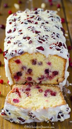 a loaf of cranberry bread with white icing on a wooden table next to some cranberries