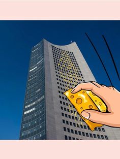 a hand holding a piece of cheese in front of a tall building