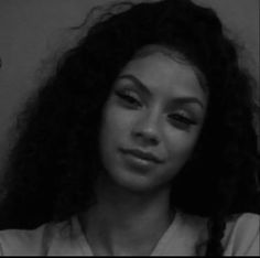 a black and white photo of a woman with long curly hair looking at the camera